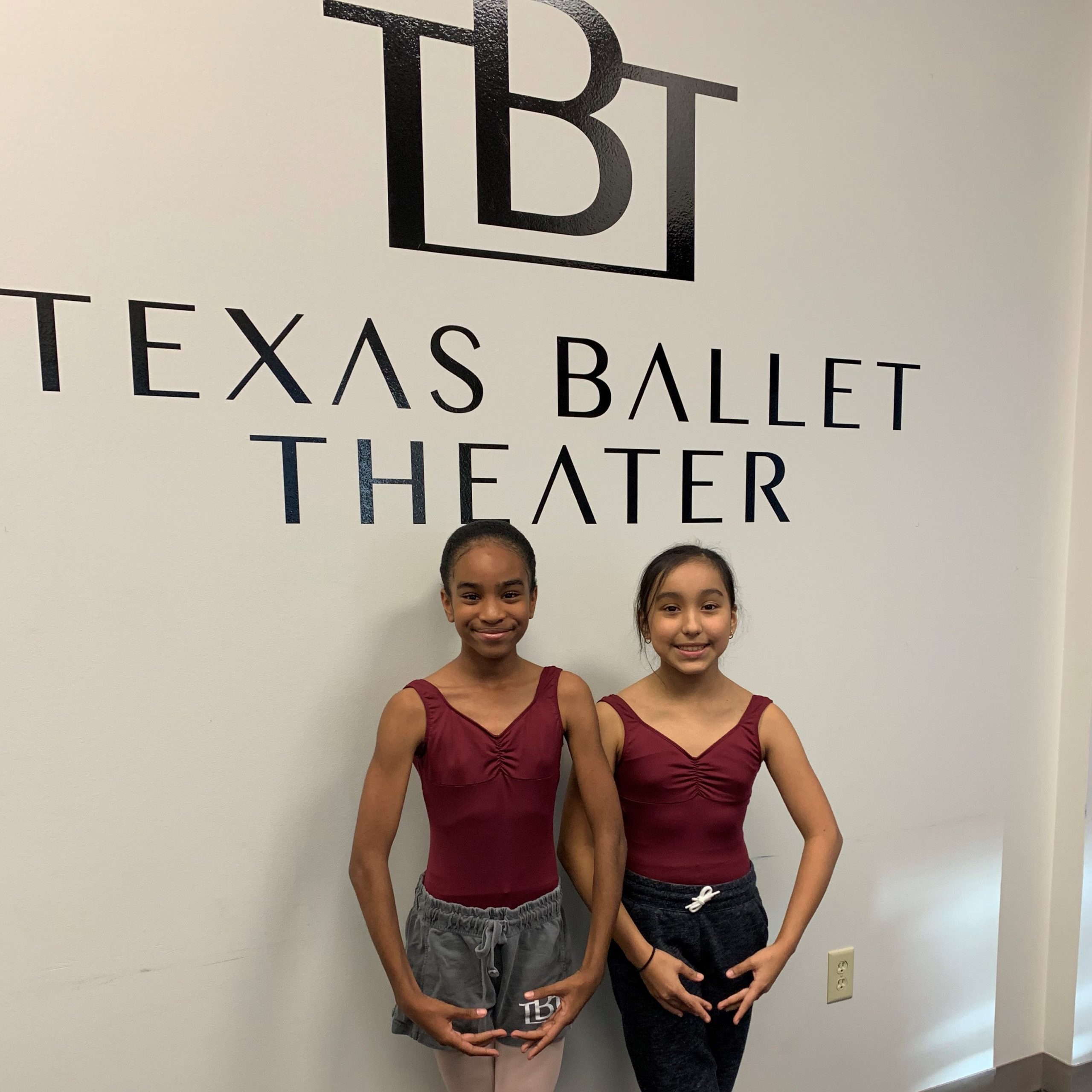 Two young female dancers posed in front of the Texas Ballet Theater logo