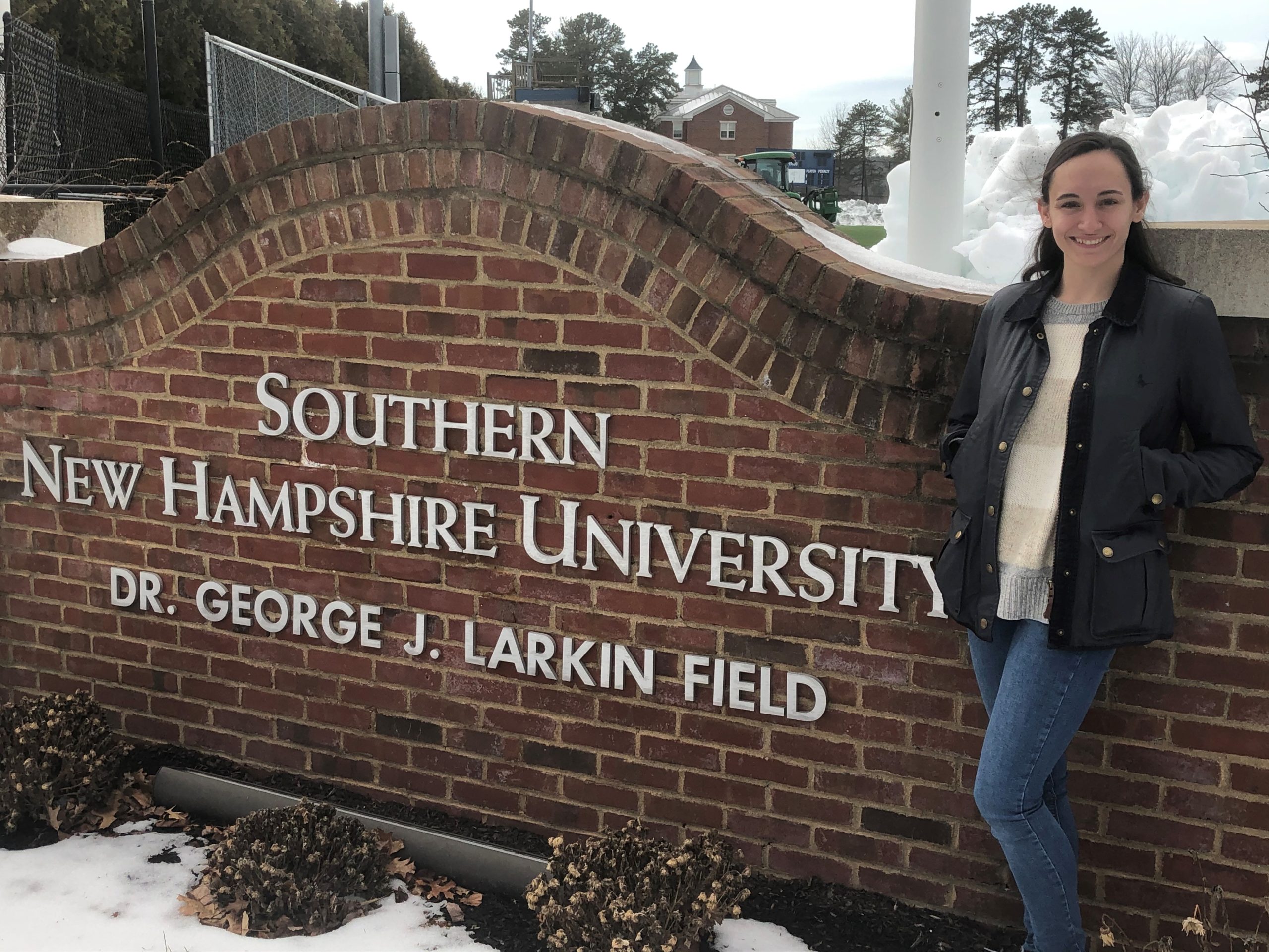 Company Dancer Cara Shipman standing next to outdoor sign reading "Southern New Hampshire University"