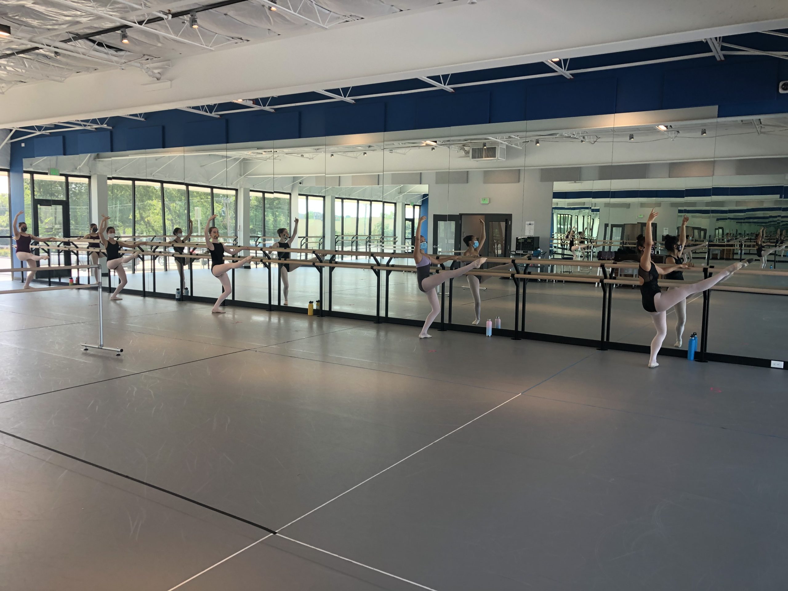 Ballet students in class, wearing masks and socially distanced at the barre.
