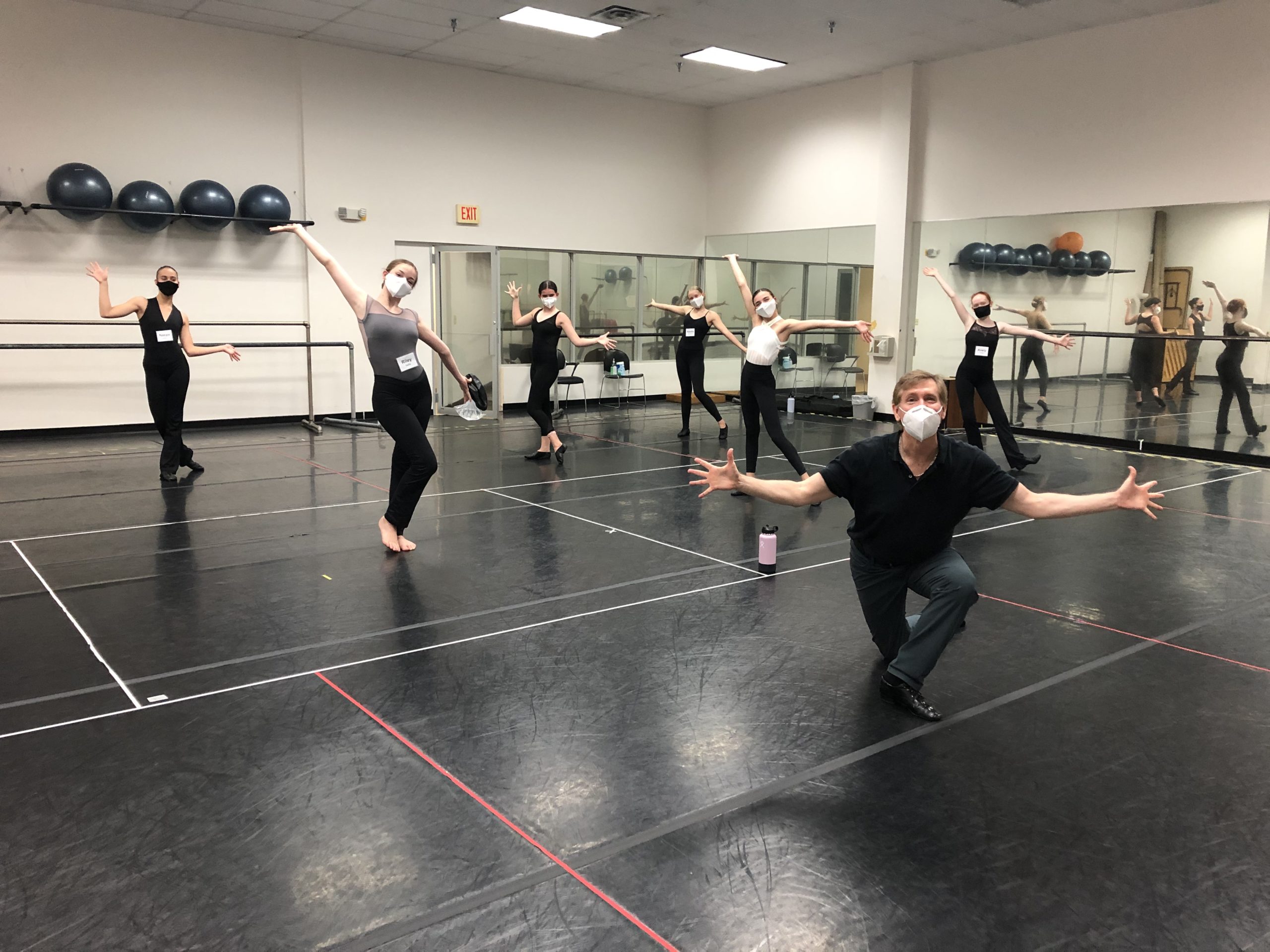 Dance students and instructor wearing masks and socially distanced in the center of a studio.