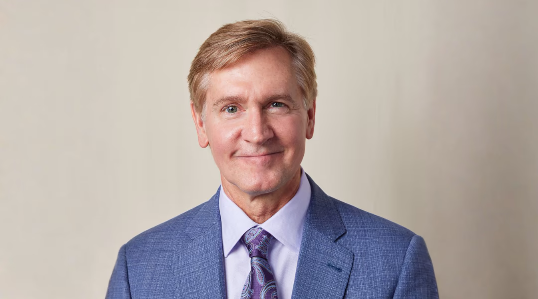 Texas Ballet Theater Artistic Director Tim O’Keefe wearing a blue textured blazer and purple paisley tie, photographed against a neutral beige background